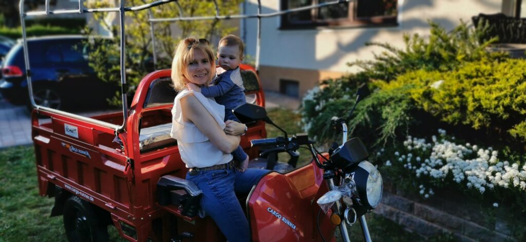 Eine Frau hält ihr Kind im Arm während Sie auf einem roten Cargo Runner Modell posiert